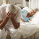 Worried Senior Man Sits On Bed Whilst Wife Sleeps
